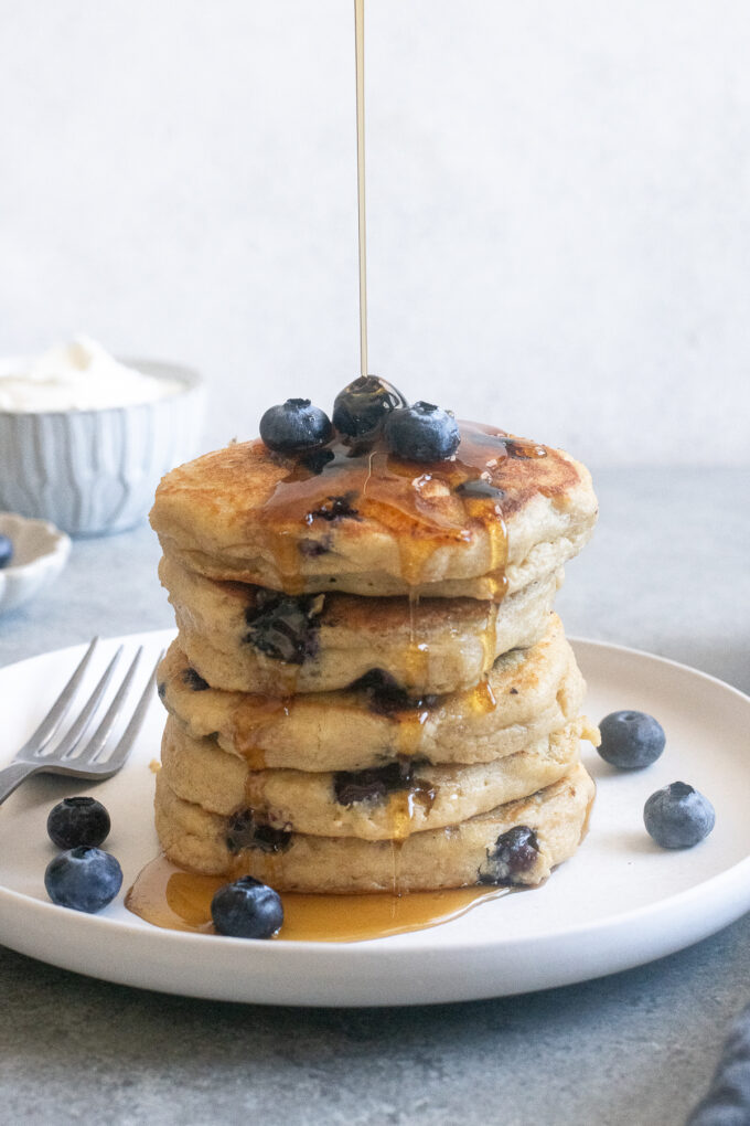 Stack of Blueberry Greek Yogurt Pancakes with syrup pouring over the top.