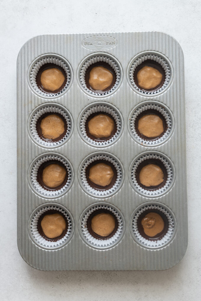 Muffin pan with peanut butter filling in dark chocolate for peanut butter cups.