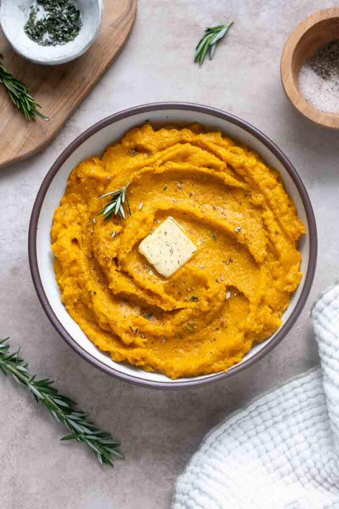 Kabocha mash in a serving bowl with butter and rosemary garnish.