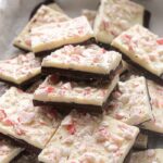 Peppermint bark squares in a parchment lined white box.