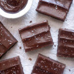 Sliced chocolate ganache brownies topped with flaky sea salt on parchment paper.