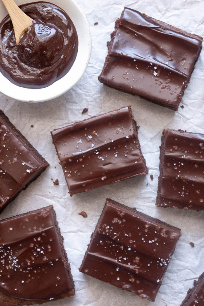Sliced chocolate ganache brownies topped with flaky sea salt on parchment paper.