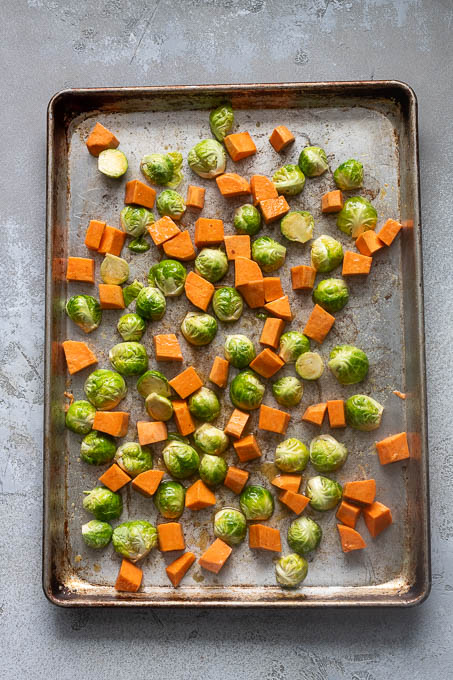 Brussels sprouts and sweet potatoes on a baking sheet before roasting.