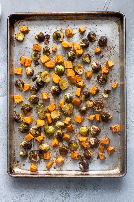 Brussels sprouts and sweet potatoes on a baking sheet after roasting.