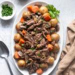 Slow cooker pot roast on a platter with potatoes and carrots.