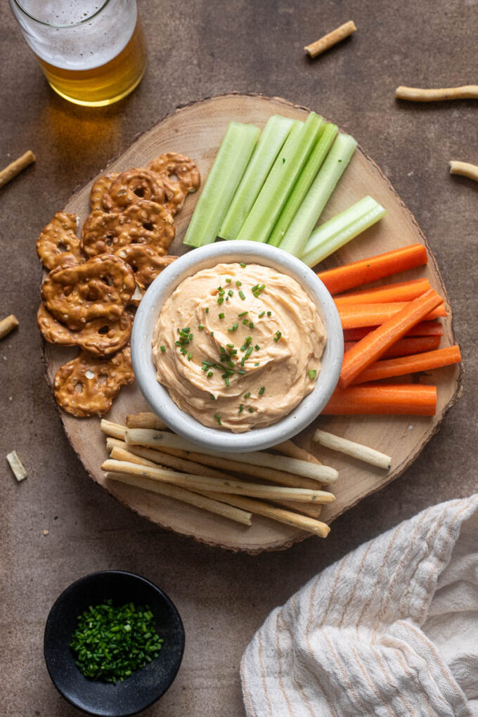 White cheddar pub cheese on a board with veggies and pretzels.
