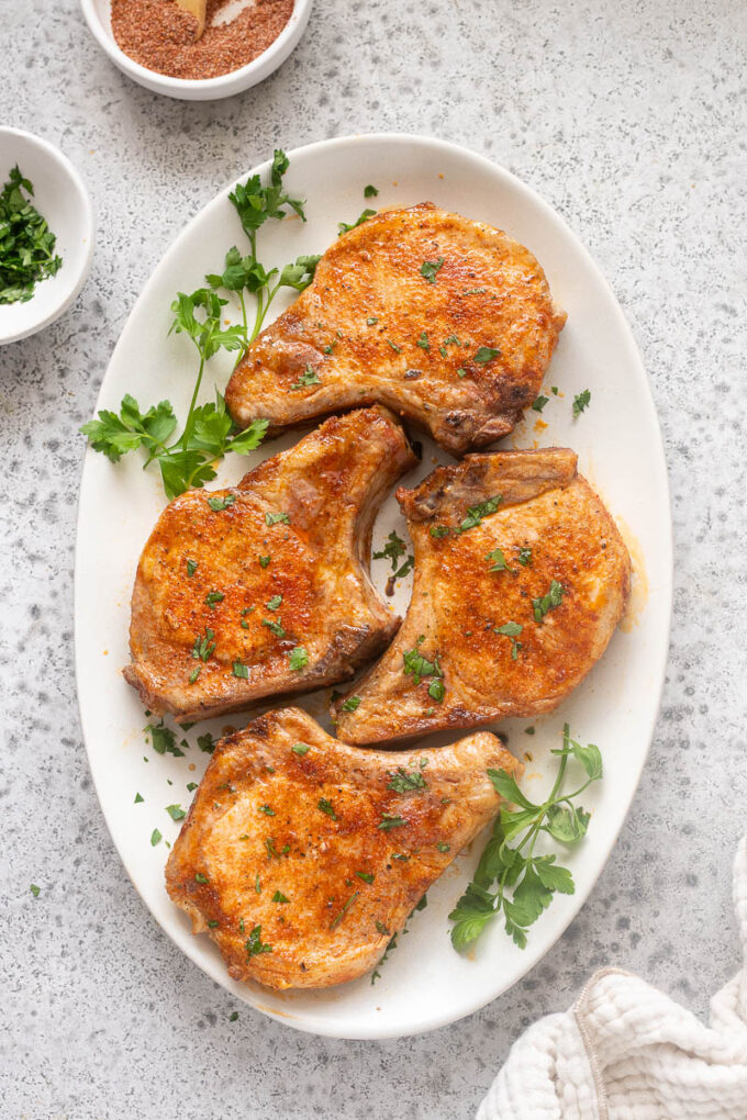 Baked bone-in pork chops on a serving platter with parsley.