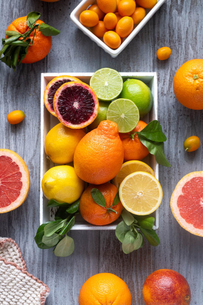 Assorted citrus fruits including blood oranges, lemons, limes and mandarins in a wooden crate.