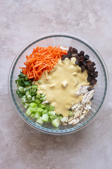 Creamy curry dressing in bowl with curry chicken salad ingredients before mixing.