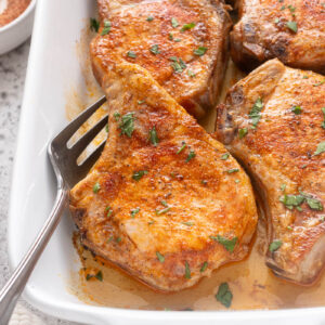 Oven baked pork chops in baking dish with serving fork.