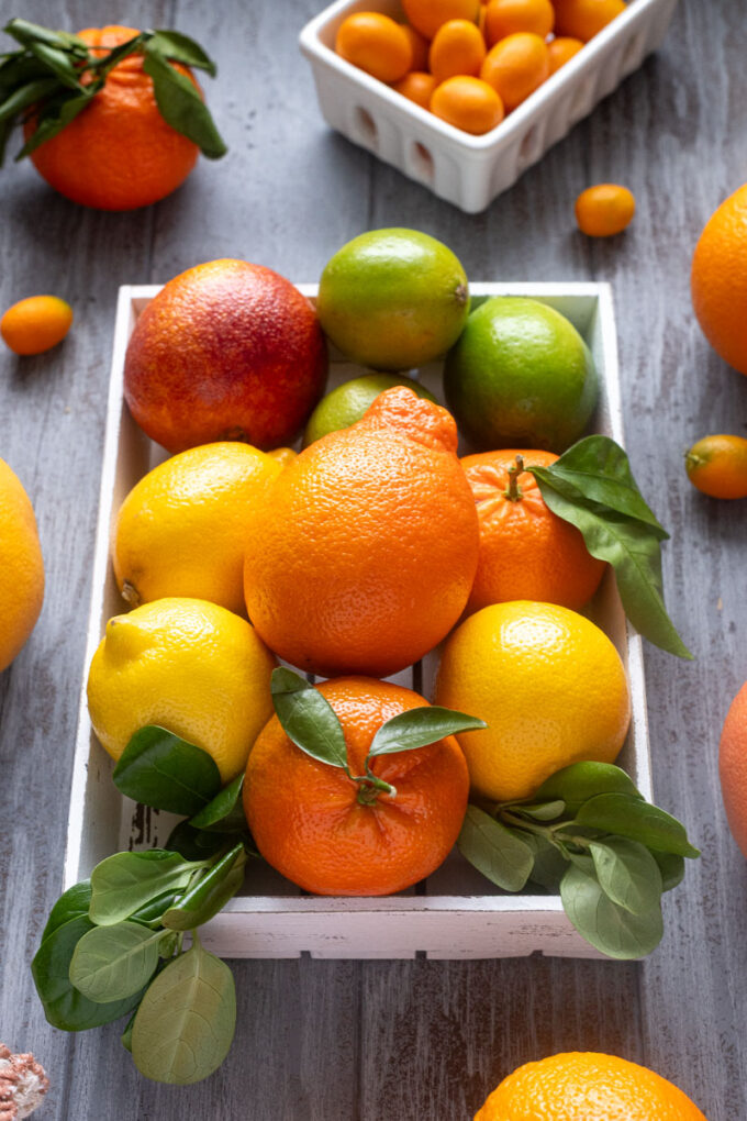 Close-up of citrus fruits in a white crate including grapefruit, blood orange, lemon and lime.