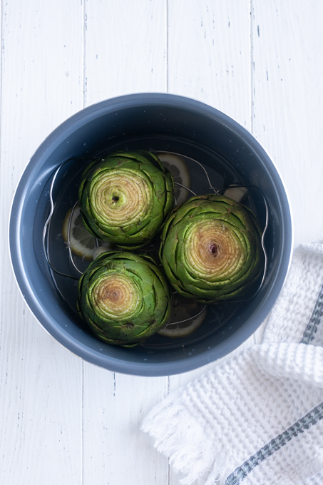 Fresh artichokes on trivet in Instant Pot before cooking.