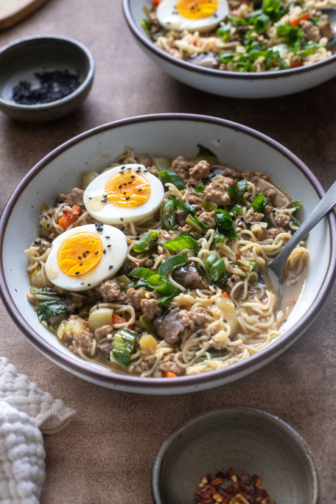 Close-up of brothy ground pork ramen with brown rice noodles and soft boiled egg.