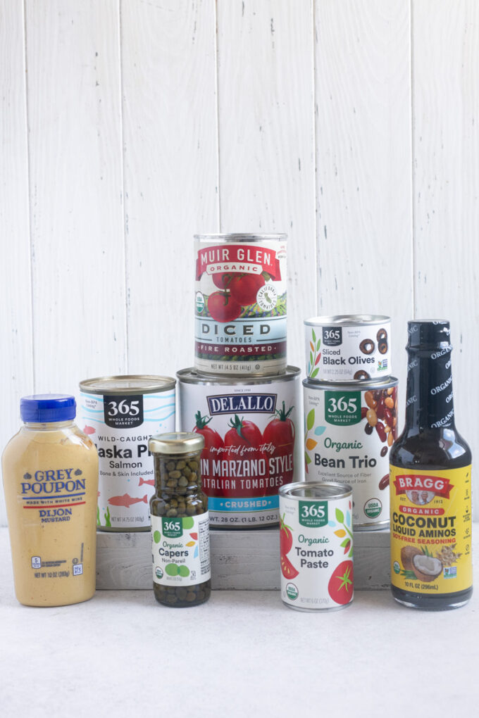 Pantry staples including tomato sauce, tomato paste, Dijon mustard and coconut aminos.