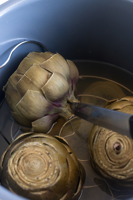 Knife inserted into bottom of artichoke to check for doneness.