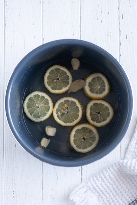 Water with lemon slices, garlic and bay leaf in bottom of Instant Pot.