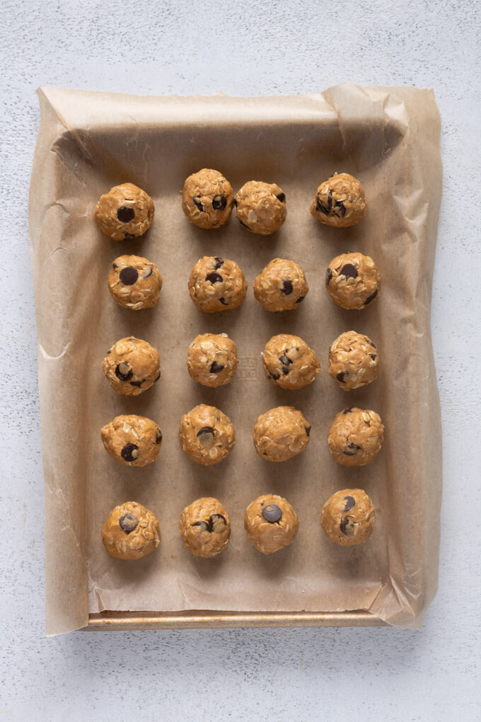 Rolled peanut butter protein balls on a parchment lined baking sheet.