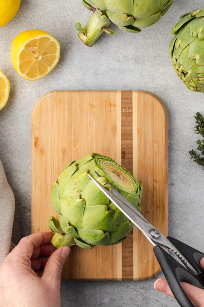 Kitchen shears trimming sharp tips from artichoke leaves.