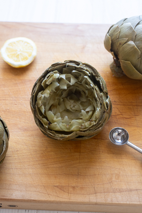 Steamed artichoke on cutting board with leaves separated.