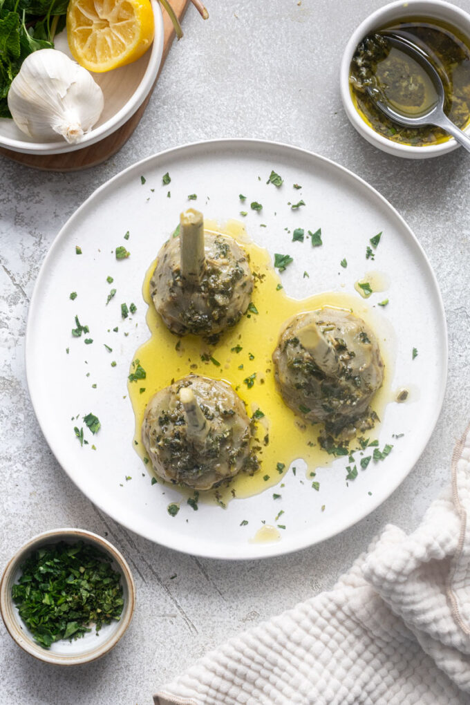 Overhead of Roman-style artichokes on a plate with olive oil herb sauce.