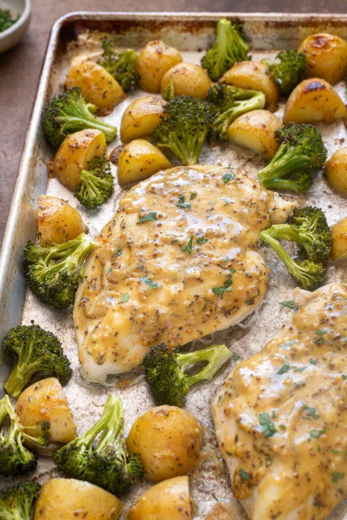 Close up honey mustard chicken breast on sheet pan with roasted vegetables.