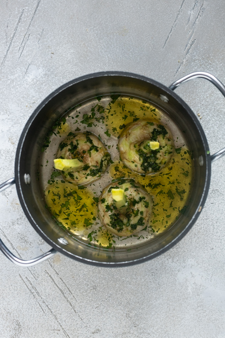 Roman artichokes in pot with garlic and herb mixture, olive oil and water.