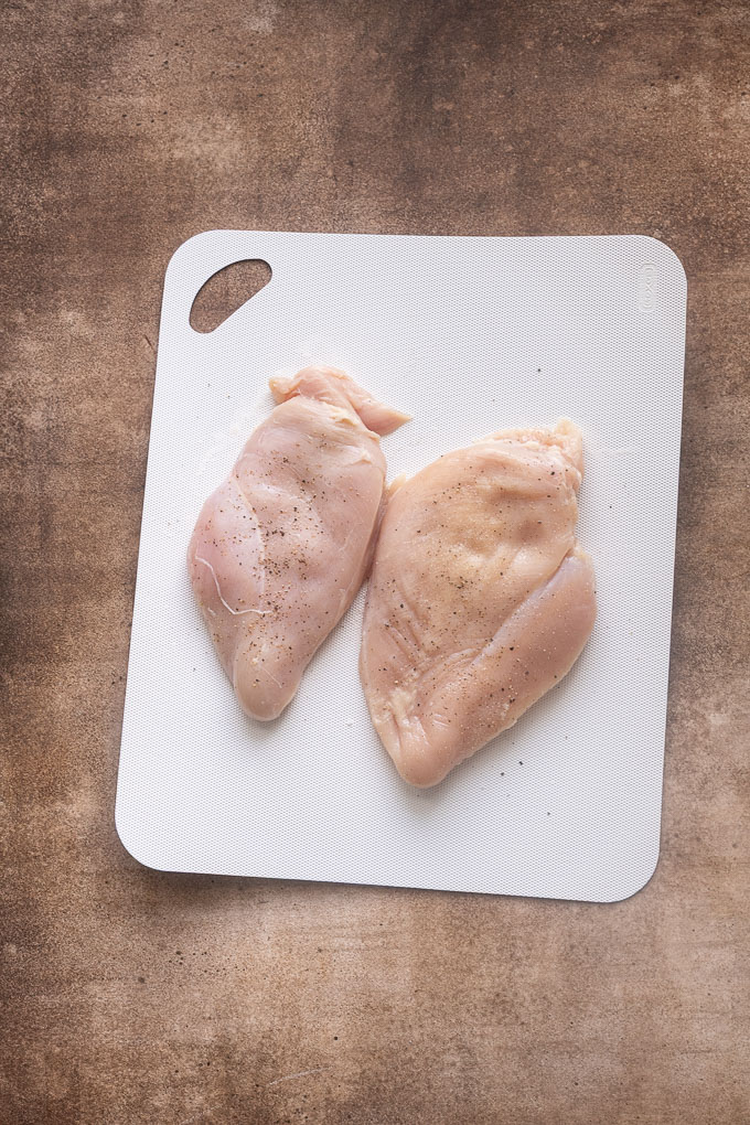 Seasoned chicken breasts for honey mustard chicken on a cutting board.