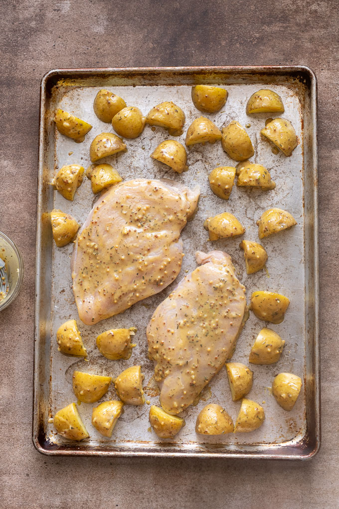 Chicken breast and potatoes brushed with honey mustard sauce on sheet pan.