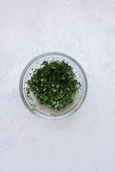 Minced garlic and chopped fresh parsley and mint in a small bowl.