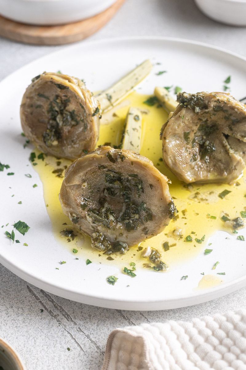 Italian braised artichokes on a plate with garlic herb olive sauce drizzled over.