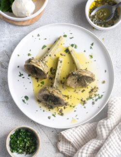 Italian braised artichokes laying sideways on a serving plate with olive oil sauce.