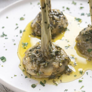 Roman artichokes on serving plate with garlic, fresh herbs and olive oil.