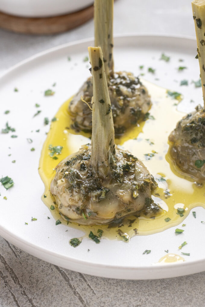 Roman artichokes on serving plate with garlic, fresh herbs and olive oil.