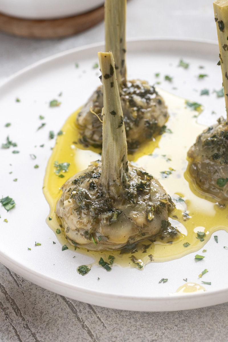 Roman artichokes on serving plate with garlic, fresh herbs and olive oil.