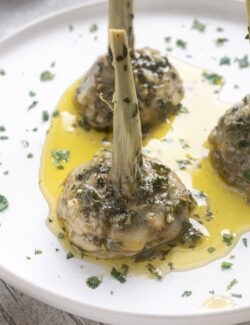 Roman-style artichokes on a white plate with fresh herb and garlic olive oil sauce.