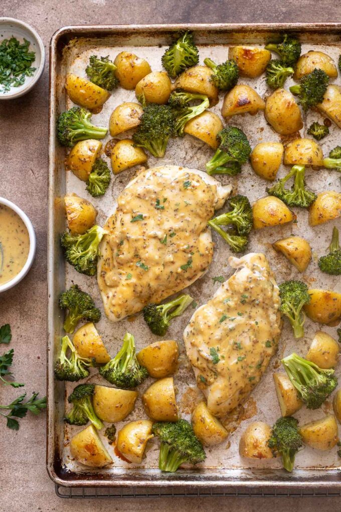 Overhead sheet pan honey mustard chicken with potatoes and broccoli.