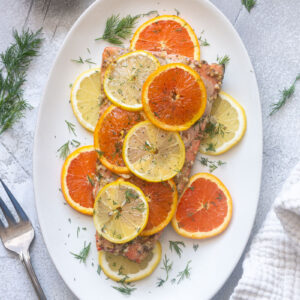Slow roasted citrus salmon with lemon, orange slices and fresh dill on a baking dish.