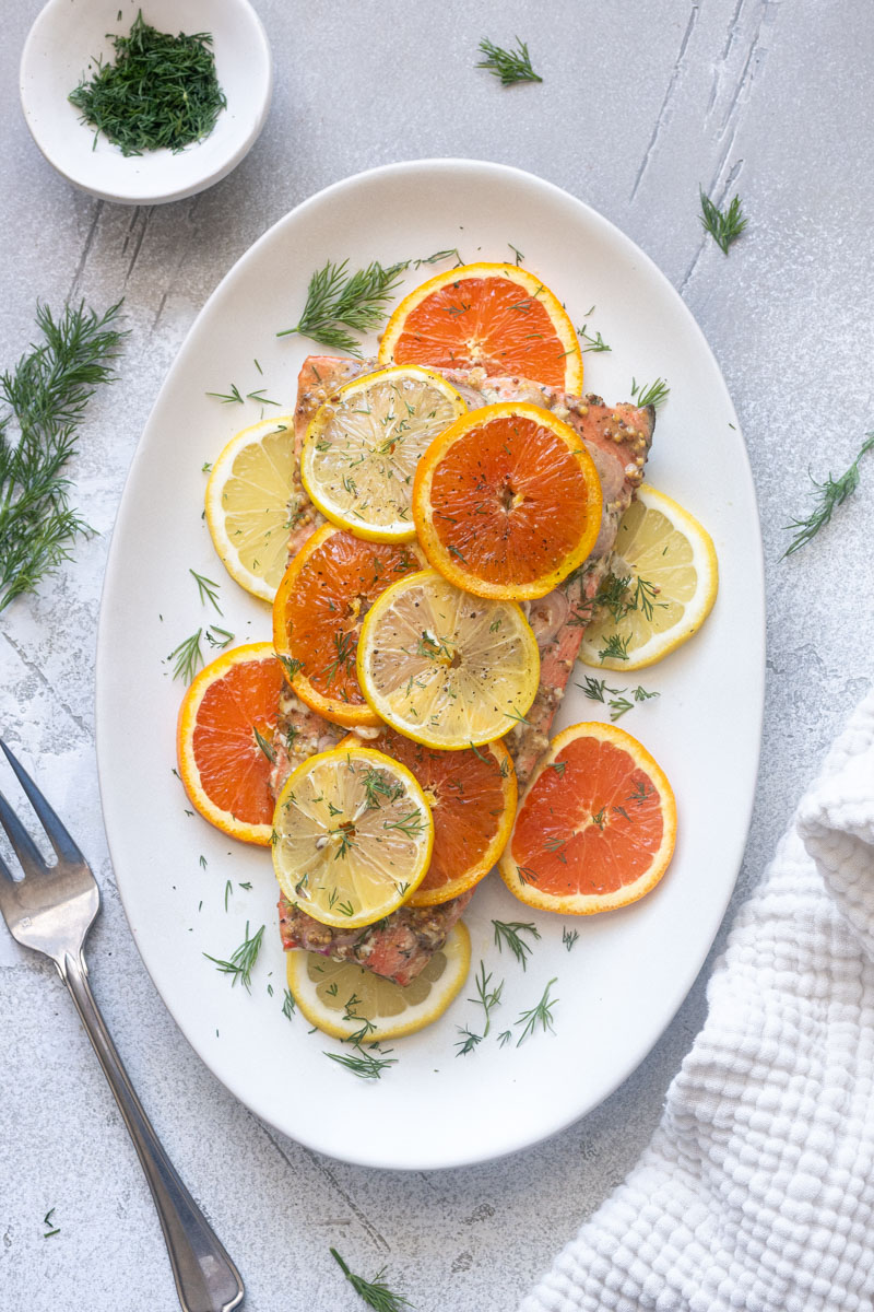 Slow roasted citrus salmon with lemon, orange slices and fresh dill on a baking dish.
