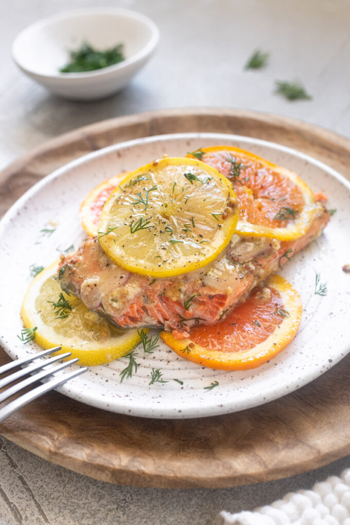 Citrus salmon on a plate with lemon and orange slices and chopped fresh dill.