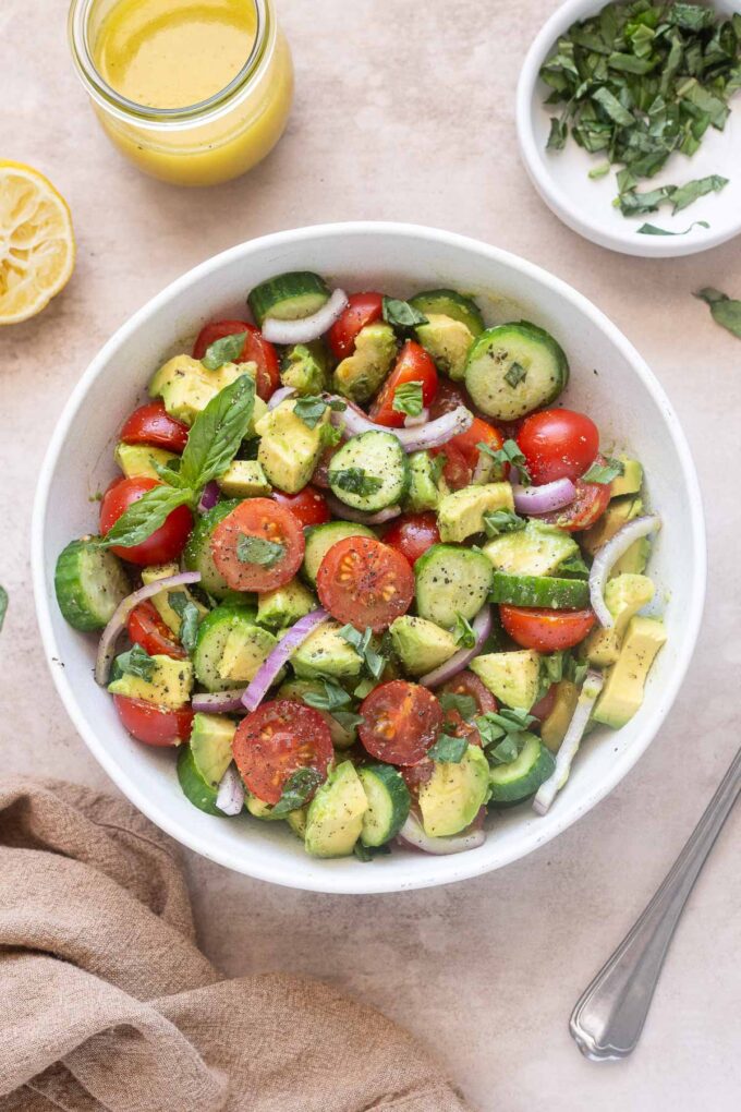 Avocado tomato and cucumber salad with basil and lemon vinaigrette in a serving bowl.