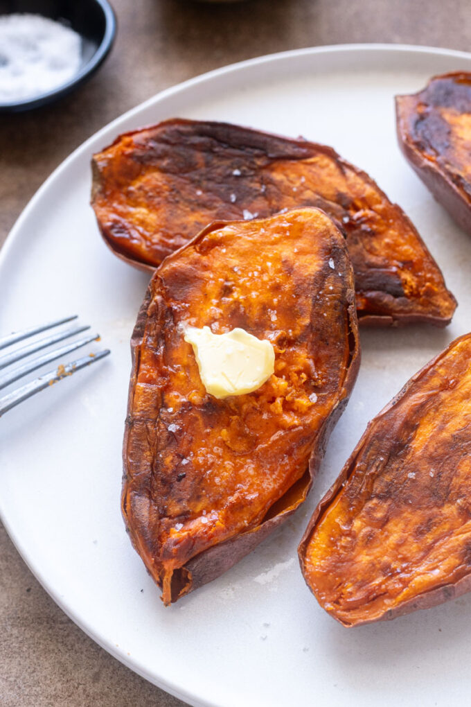 Baked sweet potato halves on a plate with butter and sea salt.