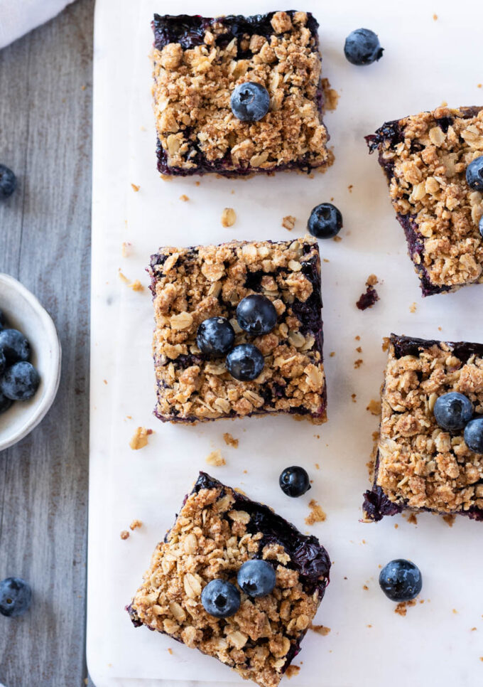 Blueberry crisp bars on a board with fresh blueberries.