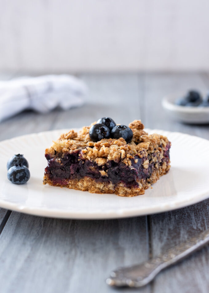 Blueberry crumble bar on a plate with fresh blueberries.