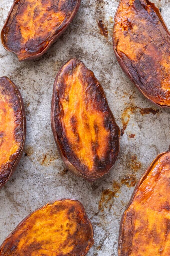 Caramelized roasted sweet potato halves on a baking sheet.