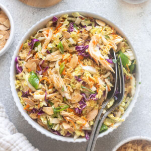 Chinese chicken salad with serving spoons digging into bowl.