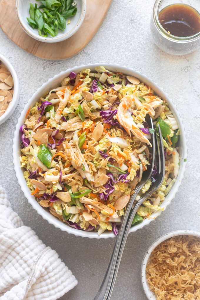 Chinese chicken salad with serving spoons digging into bowl.
