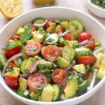 Cucumber tomato avocado salad in a bowl with basil and lemon vinaigrette.