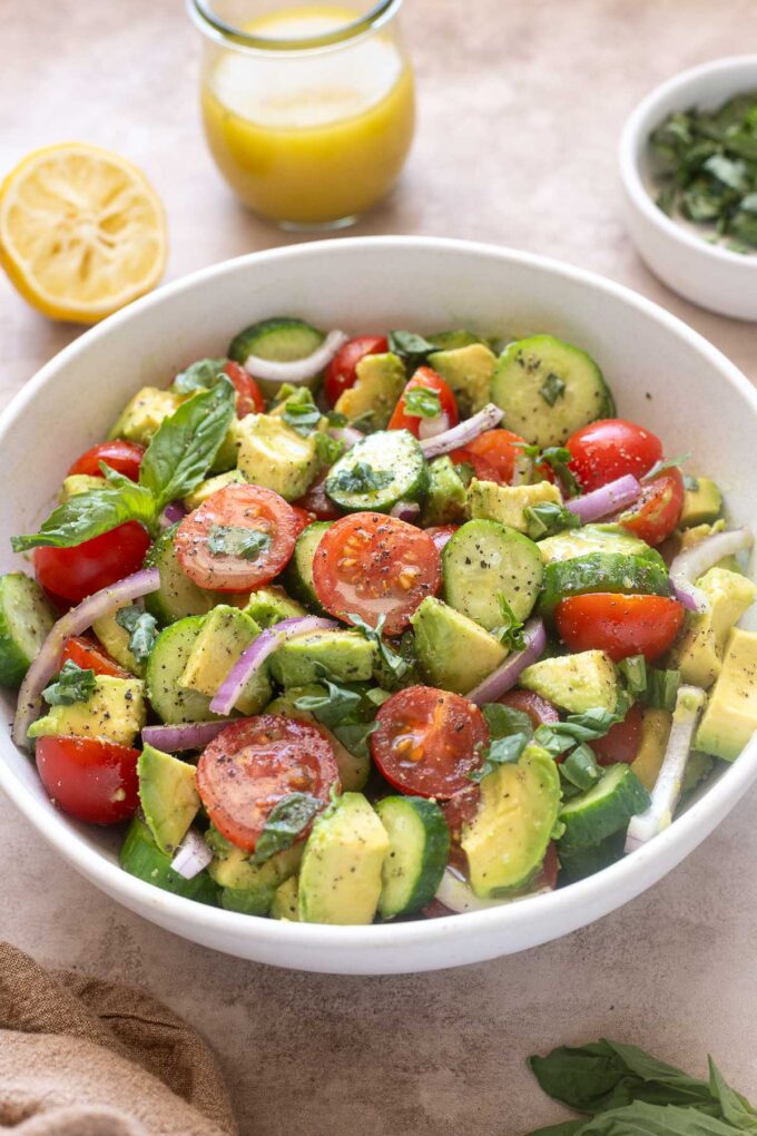 Cucumber tomato avocado salad in a bowl with basil and lemon vinaigrette.