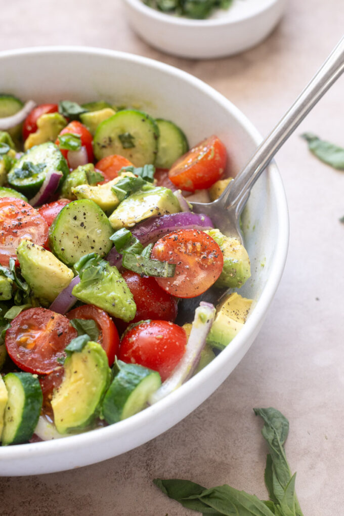 Cucumber tomato avocado salad with lemon vinaigrette in serving bowl with a spoon.