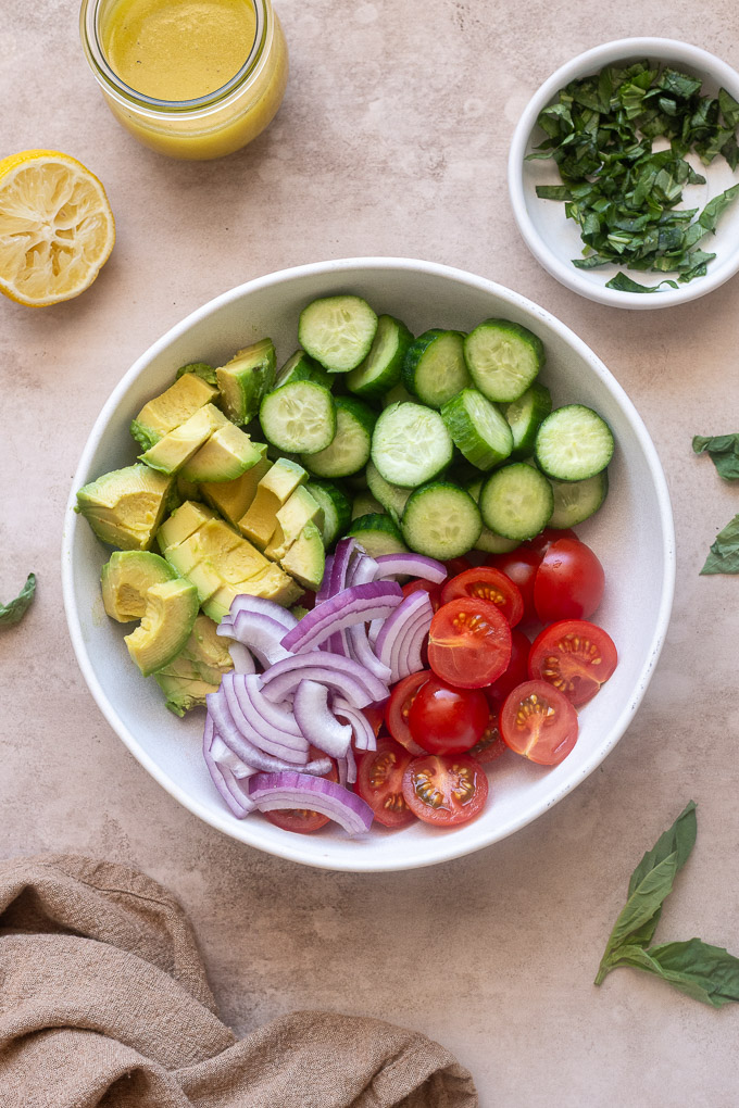 Chopped cucumbers tomatoes avocado unmixed in a bowl.